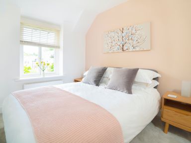 A bedroom with a bed pillows and a knitted blanket next to a window with blinds and flowers on the sill at Teviot Cottage in Corbridge