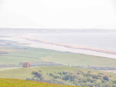 A landscape view of green fields trees a historic building and a coastline at Market House in Abbotsbury