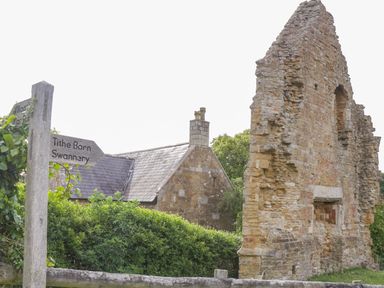 A stone building ruin next to a small house with a chimney and a wooden signpost with direction arrows at Market House in Abbotsbury