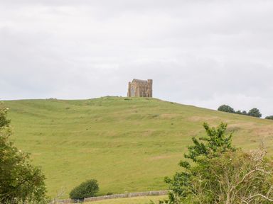 A grassy hill with a stone building on top and trees in the foreground at Market House in Abbotsbury