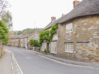 A street with stone buildings and greenery along the sidewalk at Market House in Abbotsbury