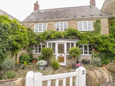 A stone house with climbing plants around windows and door with potted plants in front and a white gate at Market House in Abbotsbury