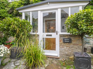 A white door with glass panels surrounded by stone walls and plants at Market House in Abbotsbury