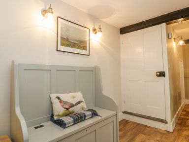 A hallway with a bench a cushion with a bird print a folded blanket wall lights a painting and a closed door at Market House in Abbotsbury