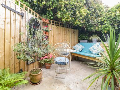 A small outdoor patio area with metal chairs and table wooden bench with cushions and various potted plants at Market House in Abbotsbury
