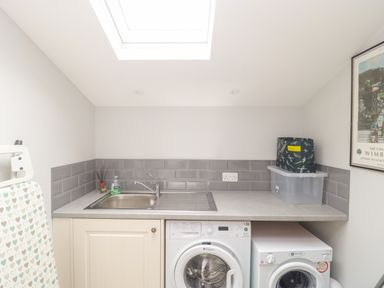 A laundry room with a sink washing machine dryer and ironing board at Market House in Abbotsbury