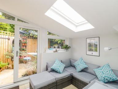 A small living room with a grey corner sofa and blue patterned cushions next to glass doors leading to a garden at Market House in Abbotsbury