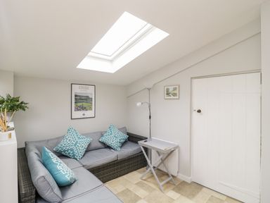 A small living room with a skylight a sectional sofa with patterned pillows a small folding table a floor lamp and two framed pictures at Market House in Abbotsbury