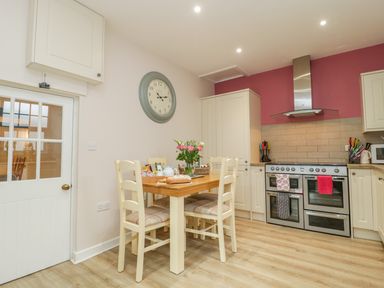 A kitchen with a wooden dining table and four chairs a wall clock and a stove with oven at Market House in Abbotsbury