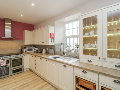 A kitchen with white cabinets a stove a sink and glassware displayed in a cabinet at Market House in Abbotsbury