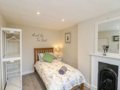 A small bedroom with a single bed a bedside table with a lamp a white shelving unit a wall mirror and a decorative fireplace at Market House in Abbotsbury