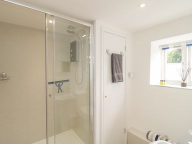 A bathroom with a glass shower enclosure a towel hanging on the door and a window with striped blinds at Market House in Abbotsbury