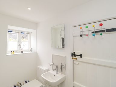 A bathroom with a toilet, sink, mirror, window, and a door with colorful hooks at Market House in Abbotsbury