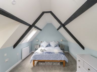 A bedroom with a bed and two bedside tables with lamps under a sloped ceiling with exposed beams at Market House in Abbotsbury