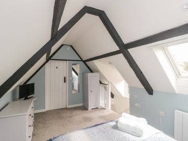A bedroom with exposed black beams white furniture a TV a wardrobe and a skylight window at Market House in Abbotsbury