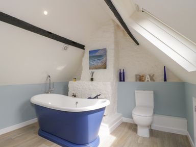 A bathroom with a blue freestanding bathtub a white toilet light wood floor and sloped ceiling at Market House in Abbotsbury