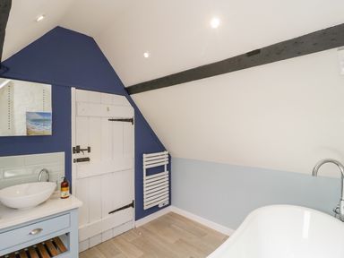 A bathroom with a white bathtub a blue and white vanity with a sink a white wooden door and a towel radiator at Market House in Abbotsbury