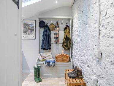 A hallway with coats hanging on hooks a wicker basket a pair of green boots a pair of brown boots on a wooden bench and a wall poster at Market House in Abbotsbury