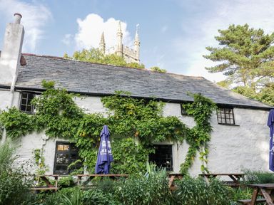 An outdoor seating area with wooden picnic tables and umbrellas in front of a white stone building with ivy and a chimney