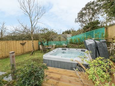 A garden with a hot tub on a wooden deck and a table with chairs near a wooden fence at Crift Farm Cottage in Lanlivery near Lostwithiel