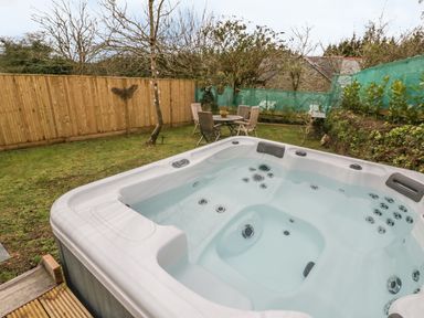 A backyard with a hot tub a wooden table with chairs grass and trees at Crift Farm Cottage Lanlivery near Lostwithiel