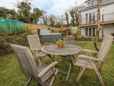 A garden with wooden table and chairs near a house with balcony and a hot tub at Crift Farm Cottage Lanlivery near Lostwithiel