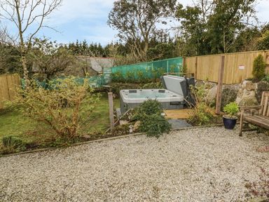 A backyard garden with a hot tub gravel area and wooden bench at Crift Farm Cottage in Lanlivery near Lostwithiel