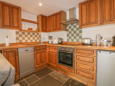 A kitchen with wooden cabinets appliances and checkered tile backsplash at Crift Farm Cottage Lanlivery near Lostwithiel