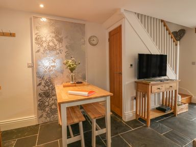 A dining area with a wooden table and benches a small wooden TV stand with a TV and stairs in the background at Crift Farm Cottage Lanlivery near Lostwithiel