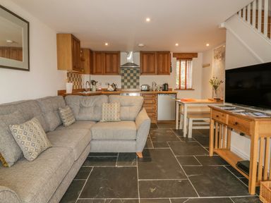An open living room and kitchen with a sectional sofa kitchen cabinets dining table and television at Crift Farm Cottage Lanlivery near Lostwithiel