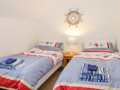 A bedroom with two single beds with blue and red bedding a wooden nightstand with a lamp and a ship wheel wall decoration at Bayside Cottage The Bay near Filey