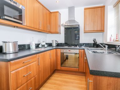 A kitchen with wooden cabinets black countertops a stainless steel oven and stove a microwave toaster kettle and sink at Bayside Cottage The Bay near Filey