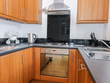 A kitchen with wooden cabinets a gas stove an oven a kettle a knife block and a sink at Bayside Cottage The Bay near Filey