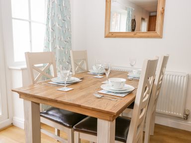 A dining table set with plates glasses and cutlery with chairs around at Bayside Cottage The Bay near Filey