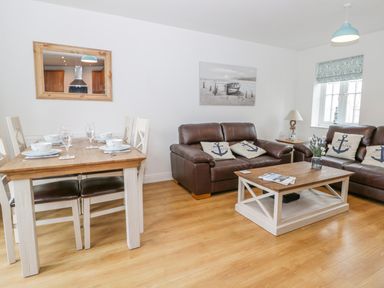 A living room with a dining table set with dishes a brown leather sofas and a wooden coffee table at Bayside Cottage in The Bay near Filey