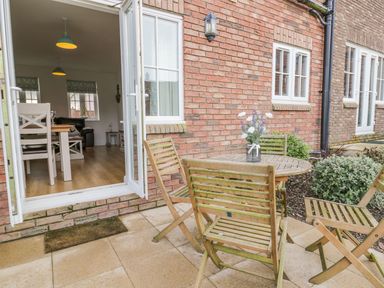 An outdoor patio with wooden table and chairs and vase with flowers next to an open door showing a dining area at Bayside Cottage The Bay near Filey