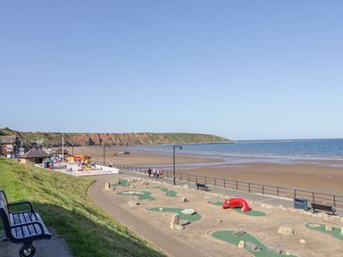 A beachside mini golf course with benches and a sandy beach with cliffs in the background at Bayside Cottage in The Bay near Filey