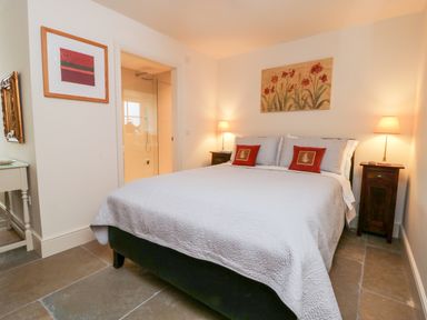 A bedroom with a double bed two bedside tables with lamps and an open door to a bathroom at Wallerthwaite Barn Cottage in Markington