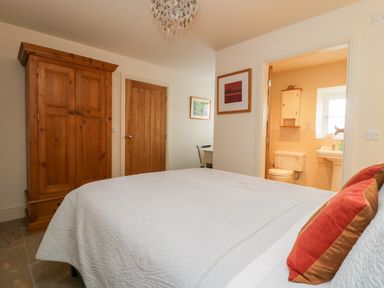 A bedroom with a white bedspread red pillows wooden wardrobe bathroom door open at Wallerthwaite Barn Cottage in Markington