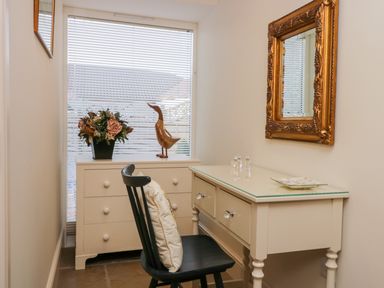 A small room with a desk and chair near a window and a dresser with decorative items at Wallerthwaite Barn Cottage in Markington