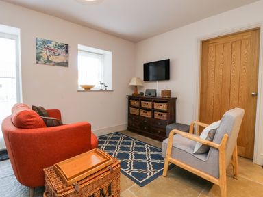 A small sitting room with an orange sofa a gray armchair a wooden cabinet with wicker baskets and a wall-mounted television at Wallerthwaite Barn Cottage in Markington