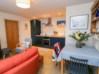 A kitchen and dining area with blue cabinets a wooden door and a table with a checked tablecloth and flowers at Wallerthwaite Barn Cottage in Markington