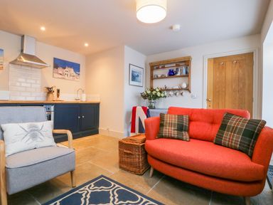 A kitchen and living area with a red sofa and armchair with cushions at Wallerthwaite Barn Cottage in Markington