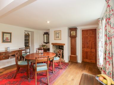 A dining room with a wooden table and chairs on a red rug a grandfather clock and floral curtains at Church View in Salisbury
