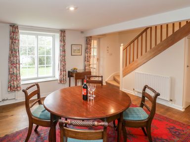 A dining room with a round wooden table and four chairs near a window with floral curtains at Church View in Salisbury