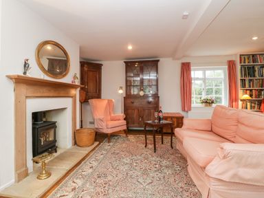 A sitting room with a fireplace a pink armchair a wooden cabinet and a pink sofa at Church View in Salisbury