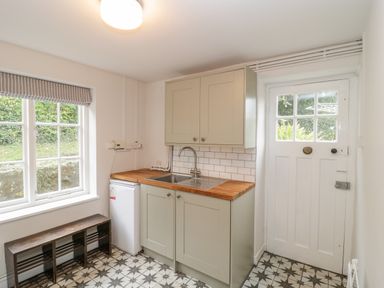 A kitchen area with a sink cabinet a small fridge a window bench and a white door at Church View in Salisbury