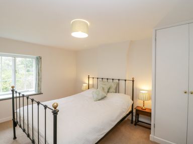 A bedroom with a bed with green pillows a window with curtains bedside tables with lamps and a built-in wardrobe at Church View in Salisbury