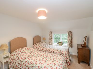 A bedroom with two single beds with floral bedspreads two bedside tables with lamps a window with floral curtains and a wooden chest of drawers with a mirror at Church View in Salisbury