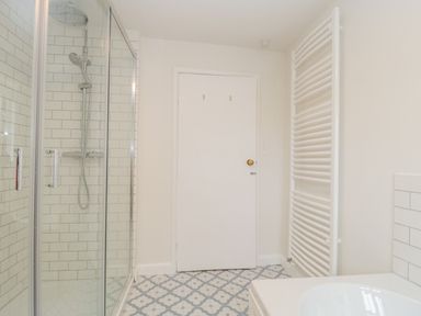 A bathroom with a glass shower enclosure a white door a white heated towel rail and patterned floor tiles at Church View in Salisbury